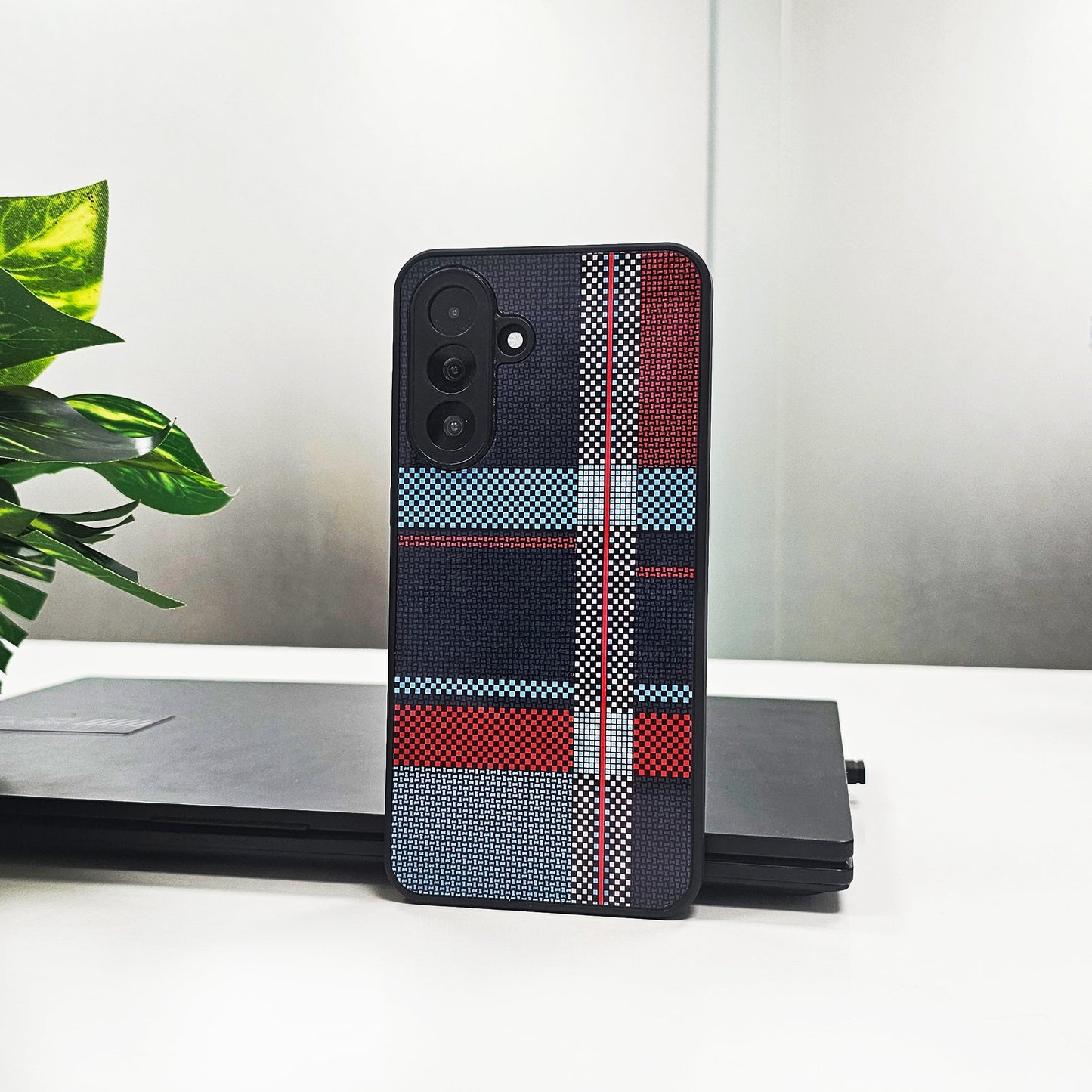 Phone case with plaid pattern on a white surface with a plant and laptop in the background